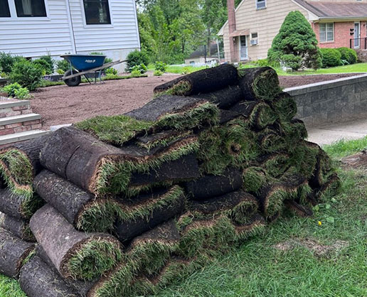 Sod rolls staged beside prepared soil for a Long Island residential sod installation project